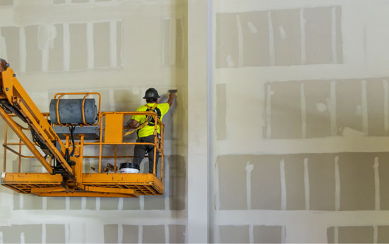 Dynamic Interiors team member on a man lift mudding & taping drywall